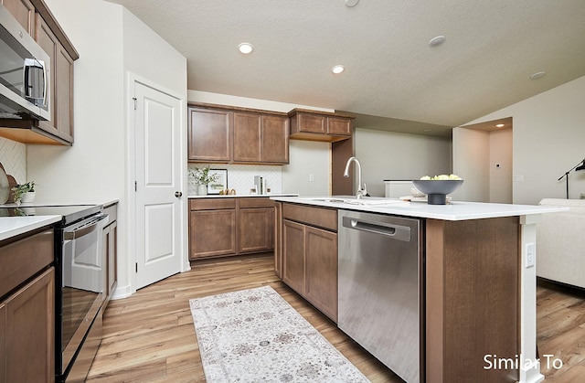 kitchen with stainless steel appliances, light hardwood / wood-style floors, sink, and a center island with sink