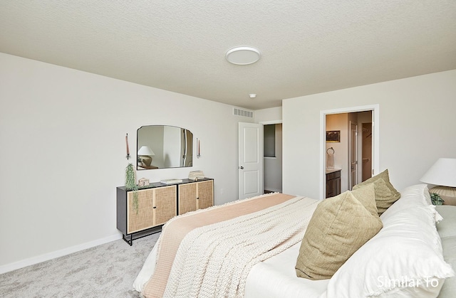 carpeted bedroom featuring ensuite bathroom and a textured ceiling