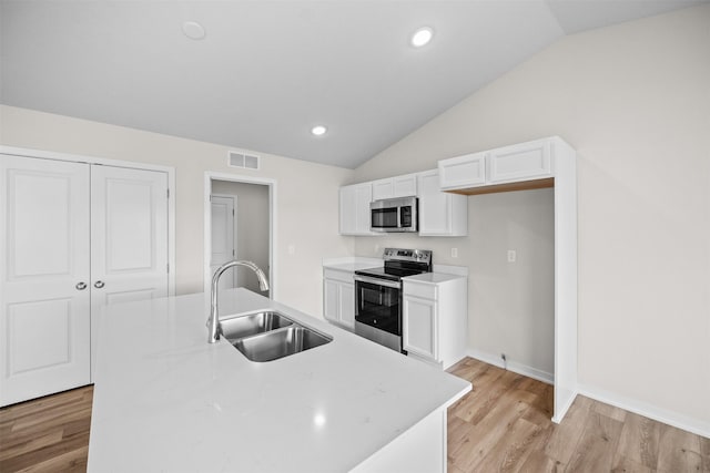 kitchen with lofted ceiling, sink, appliances with stainless steel finishes, a kitchen island with sink, and white cabinets