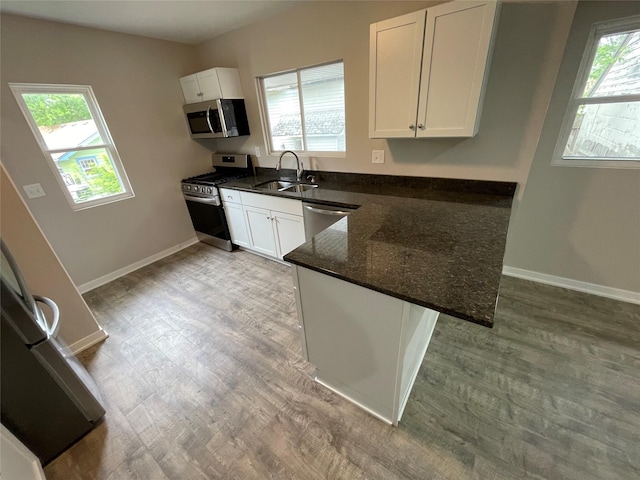 kitchen with sink, white cabinetry, dark stone countertops, stainless steel appliances, and hardwood / wood-style floors