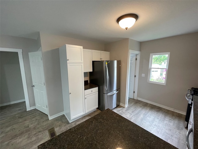 kitchen with stainless steel appliances, dark stone counters, wood-type flooring, and white cabinets