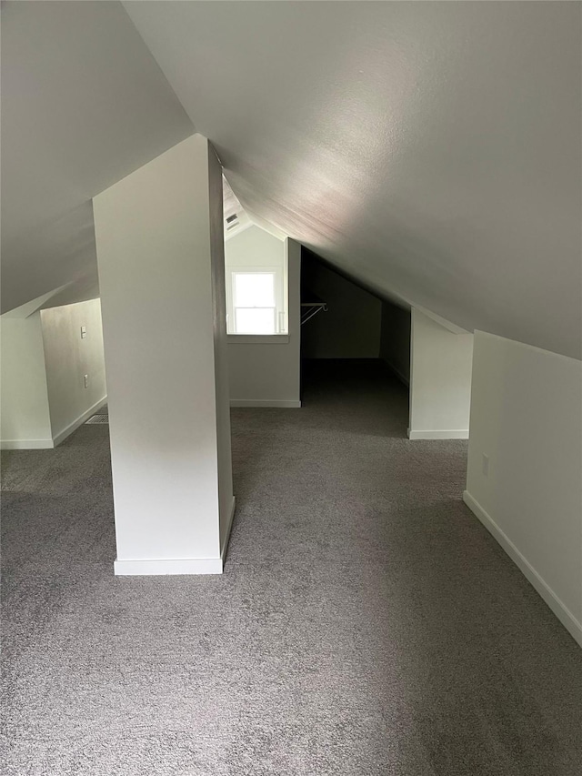 bonus room with dark colored carpet and vaulted ceiling