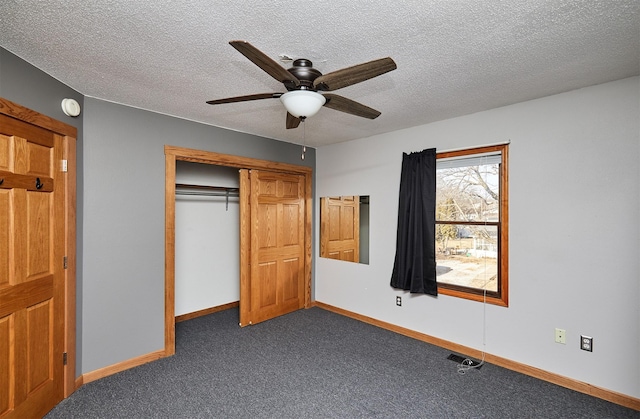 unfurnished bedroom with ceiling fan, a textured ceiling, dark carpet, and a closet