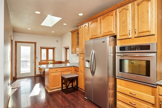 kitchen featuring appliances with stainless steel finishes, a skylight, a textured ceiling, dark hardwood / wood-style flooring, and kitchen peninsula