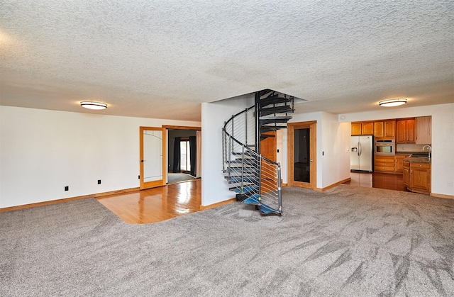 unfurnished living room featuring light colored carpet, sink, and a textured ceiling