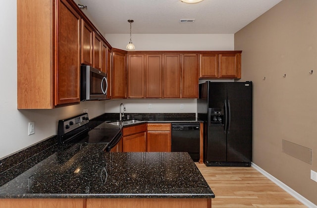 kitchen featuring sink, dark stone countertops, kitchen peninsula, pendant lighting, and black appliances