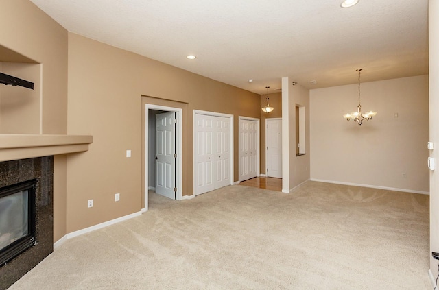 unfurnished living room featuring an inviting chandelier, light carpet, and a high end fireplace