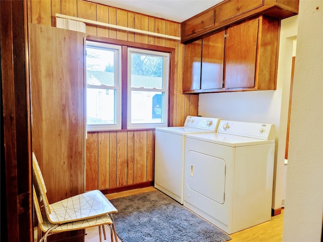 laundry room with cabinets, washer and dryer, light wood-type flooring, and wood walls