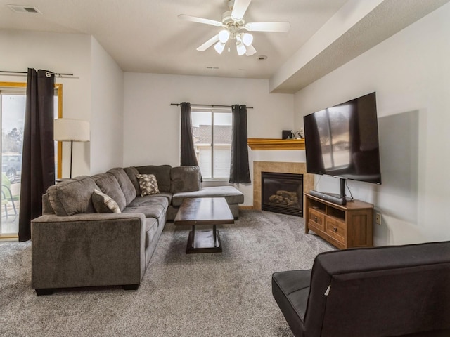 living room with ceiling fan, carpet flooring, and a tiled fireplace