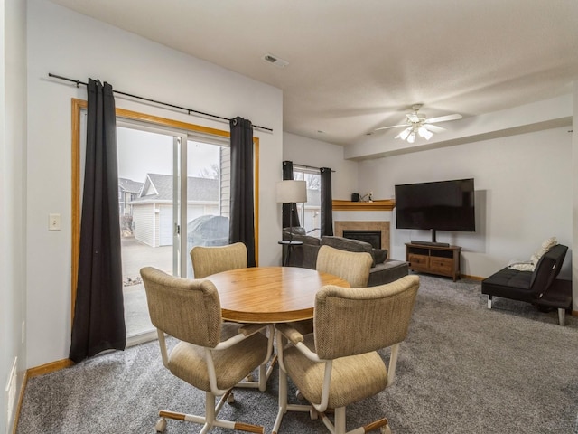 carpeted dining space with a fireplace and ceiling fan