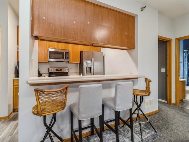 kitchen featuring carpet floors, a kitchen breakfast bar, kitchen peninsula, and appliances with stainless steel finishes