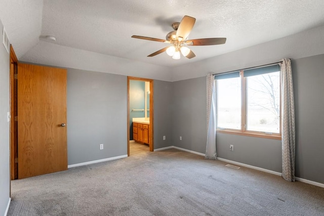 unfurnished bedroom featuring ceiling fan, ensuite bathroom, light carpet, and a textured ceiling