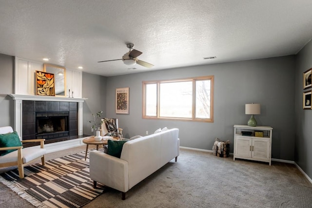 living room with ceiling fan, a tiled fireplace, carpet, and a textured ceiling