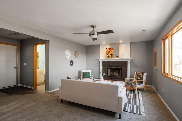 carpeted living room with ceiling fan, a tile fireplace, and a textured ceiling