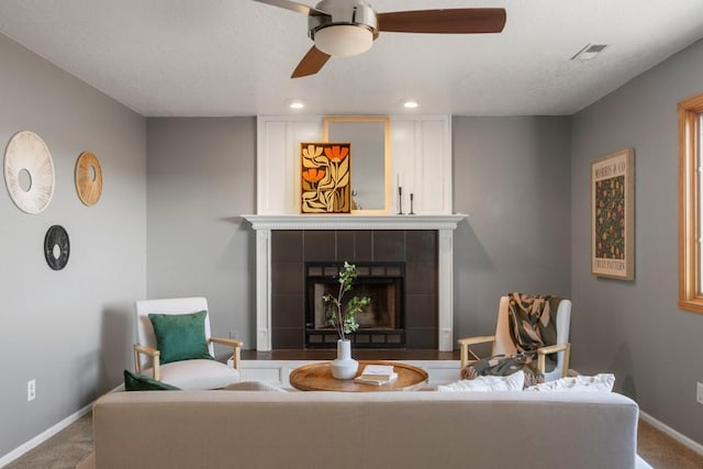 living room featuring a tile fireplace, carpet floors, and ceiling fan