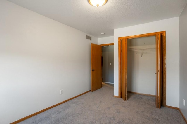 unfurnished bedroom with light colored carpet, a closet, and a textured ceiling