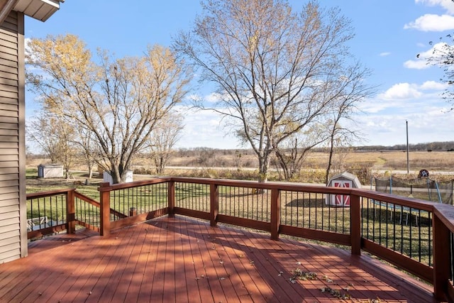 wooden deck featuring a storage shed, a trampoline, and a rural view