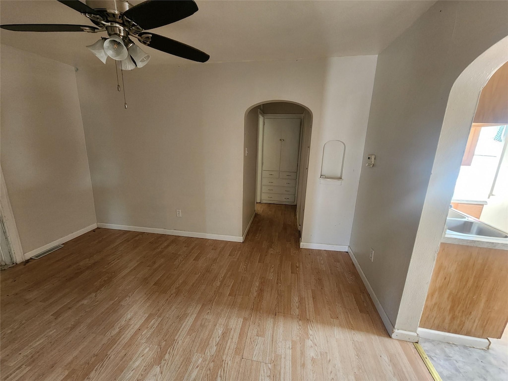 unfurnished room with baseboards, visible vents, arched walkways, ceiling fan, and light wood-style floors