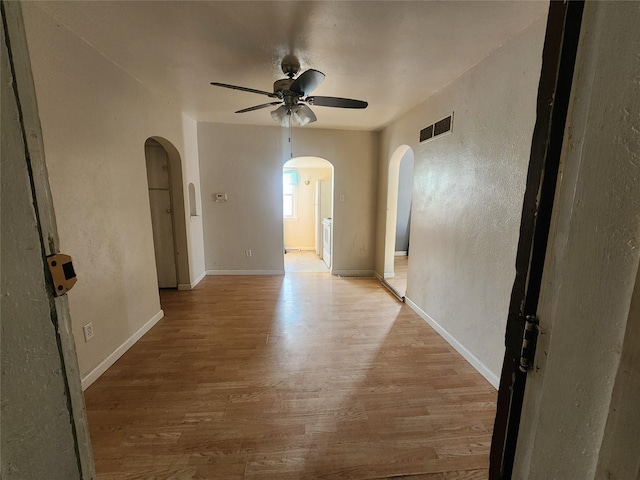 unfurnished room with arched walkways, light wood finished floors, visible vents, and a ceiling fan