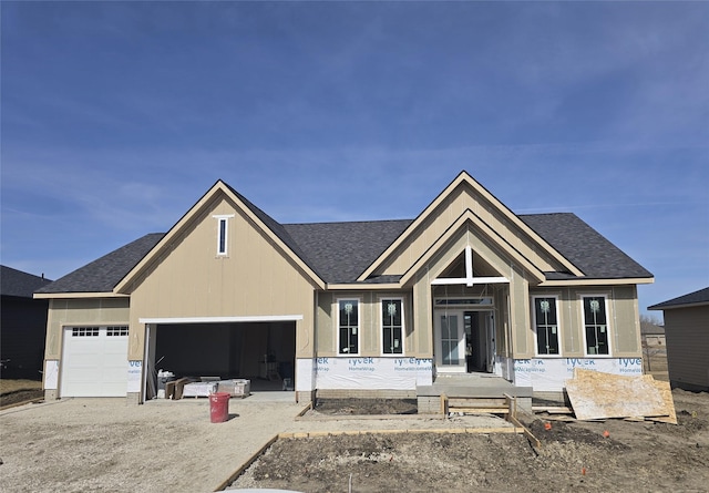 unfinished property featuring gravel driveway, an attached garage, and roof with shingles