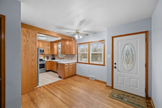 kitchen featuring sink, decorative backsplash, ceiling fan, stainless steel appliances, and light hardwood / wood-style flooring