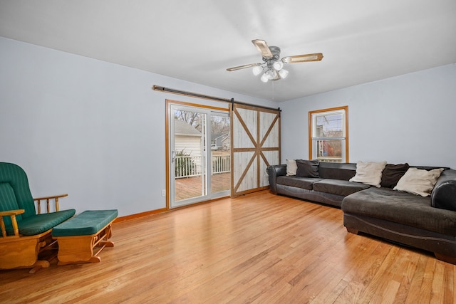 living room with ceiling fan, a barn door, and light hardwood / wood-style flooring