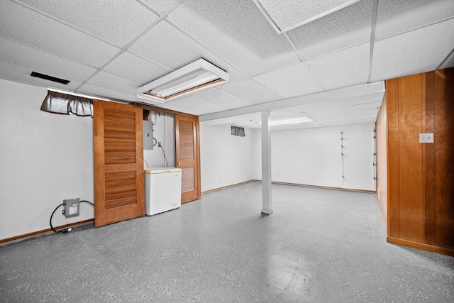 basement with a paneled ceiling, fridge, and electric panel