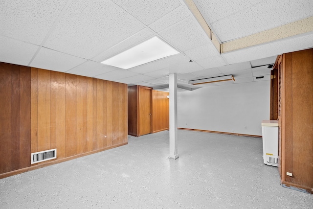 basement featuring a paneled ceiling and wooden walls