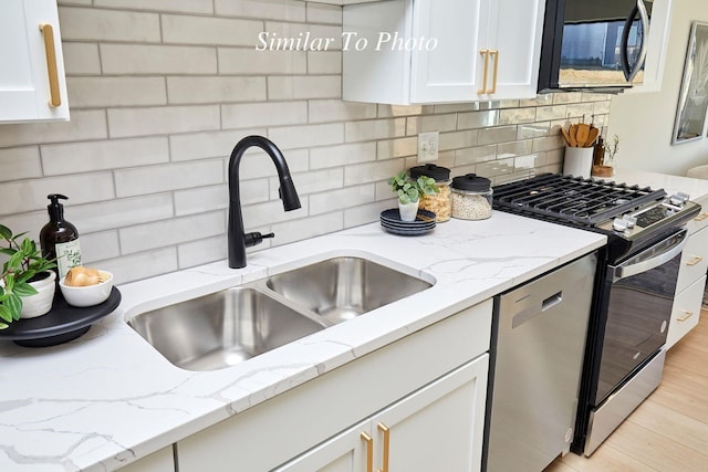kitchen with tasteful backsplash, light stone countertops, appliances with stainless steel finishes, white cabinets, and a sink