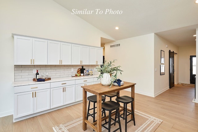 kitchen featuring visible vents, backsplash, light countertops, lofted ceiling, and light wood-style floors