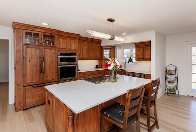 kitchen featuring sink, appliances with stainless steel finishes, a kitchen island, decorative light fixtures, and light wood-type flooring