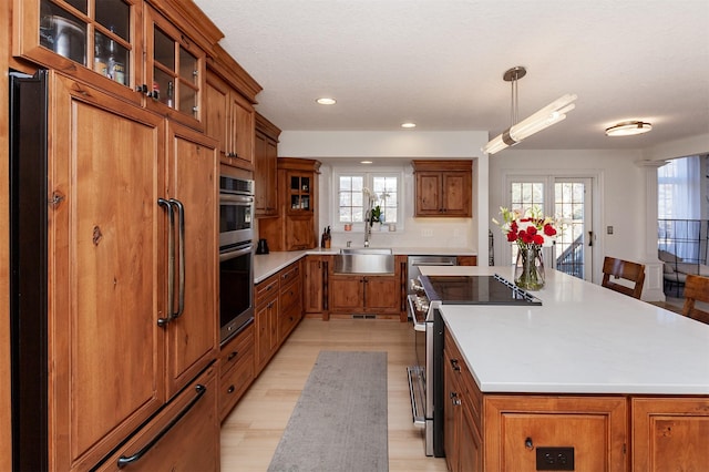 kitchen with sink, decorative light fixtures, a center island, appliances with stainless steel finishes, and light hardwood / wood-style floors