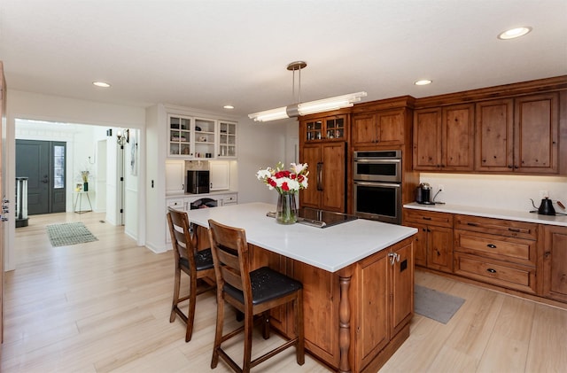 kitchen with a breakfast bar, double oven, decorative light fixtures, a center island, and light wood-type flooring