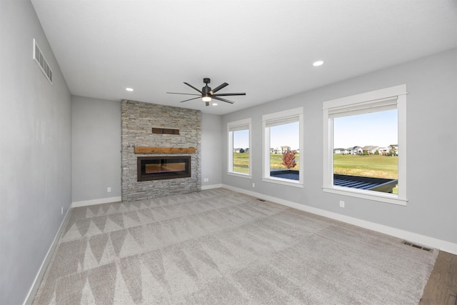 unfurnished living room featuring ceiling fan, a stone fireplace, and light colored carpet