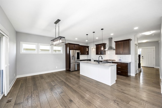 kitchen featuring wall chimney exhaust hood, decorative light fixtures, dark hardwood / wood-style floors, stainless steel appliances, and a kitchen island with sink