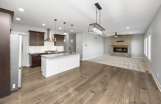 kitchen featuring pendant lighting, stainless steel fridge, a center island with sink, a barn door, and wall chimney exhaust hood