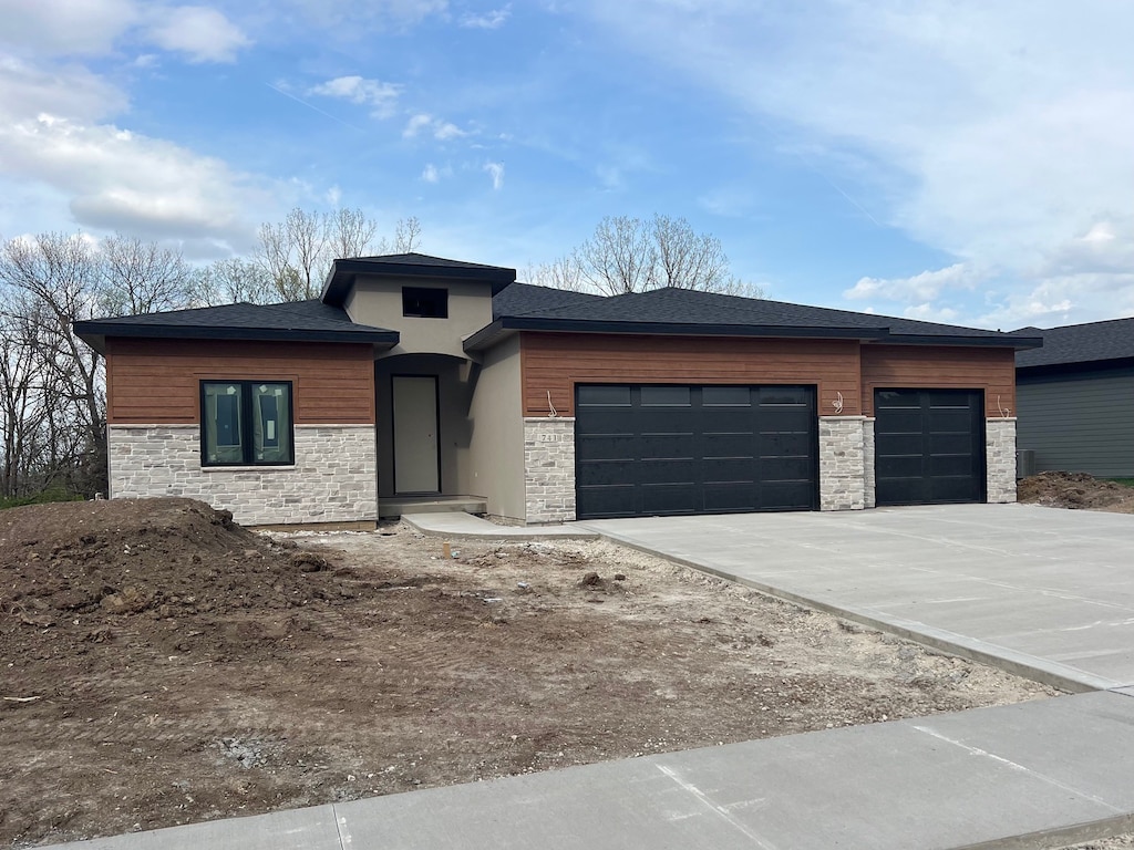 prairie-style house featuring a garage, driveway, and stone siding