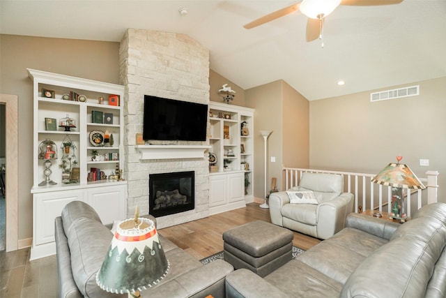 living room featuring ceiling fan, lofted ceiling, a stone fireplace, and hardwood / wood-style floors