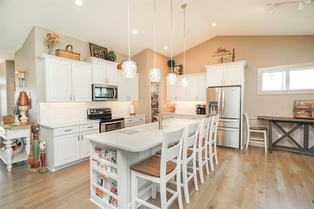 kitchen featuring a kitchen bar, pendant lighting, stainless steel appliances, a kitchen island with sink, and white cabinets