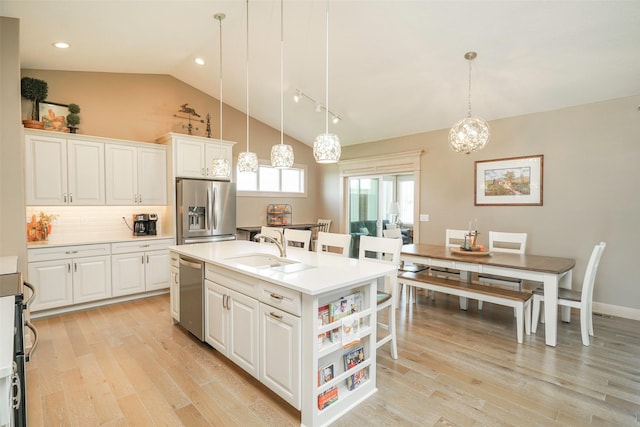 kitchen featuring hanging light fixtures, stainless steel appliances, an island with sink, white cabinets, and light wood-type flooring