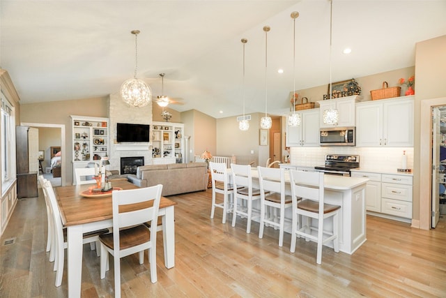 dining room featuring vaulted ceiling, a large fireplace, a chandelier, and light wood-type flooring