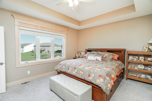 carpeted bedroom with ceiling fan and a tray ceiling