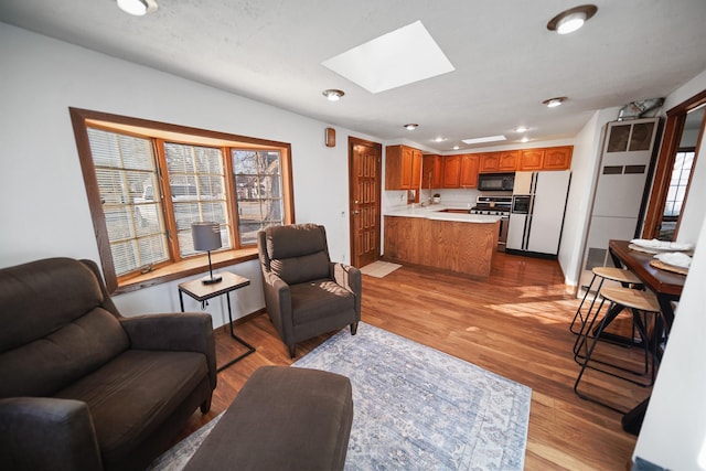 living area with baseboards, light wood-type flooring, a skylight, and recessed lighting