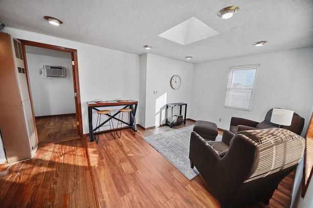 living area with a textured ceiling, a skylight, wood finished floors, baseboards, and a wall mounted air conditioner