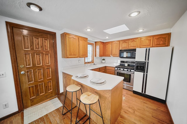 kitchen featuring a skylight, stainless steel gas range oven, white refrigerator with ice dispenser, black microwave, and a sink