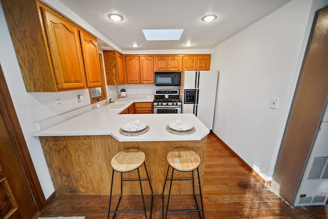 kitchen featuring stainless steel range with gas cooktop, a skylight, white refrigerator with ice dispenser, black microwave, and a peninsula