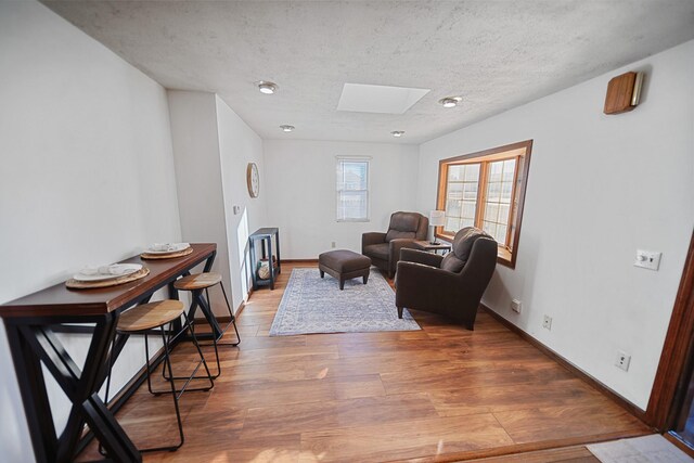 living area with a skylight, a textured ceiling, baseboards, and wood finished floors