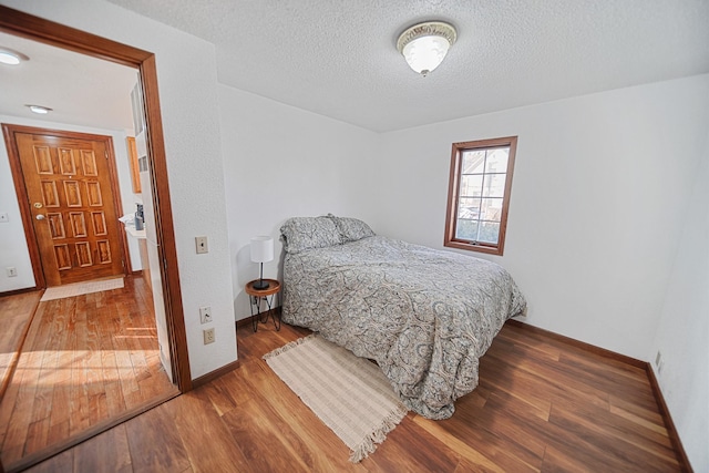 bedroom featuring a textured ceiling, baseboards, and wood finished floors