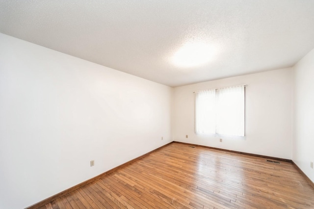 empty room with a textured ceiling and light hardwood / wood-style floors