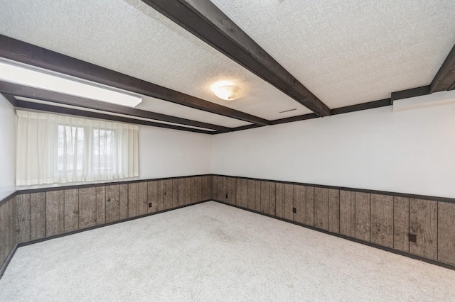 carpeted empty room with wooden walls, beam ceiling, and a textured ceiling